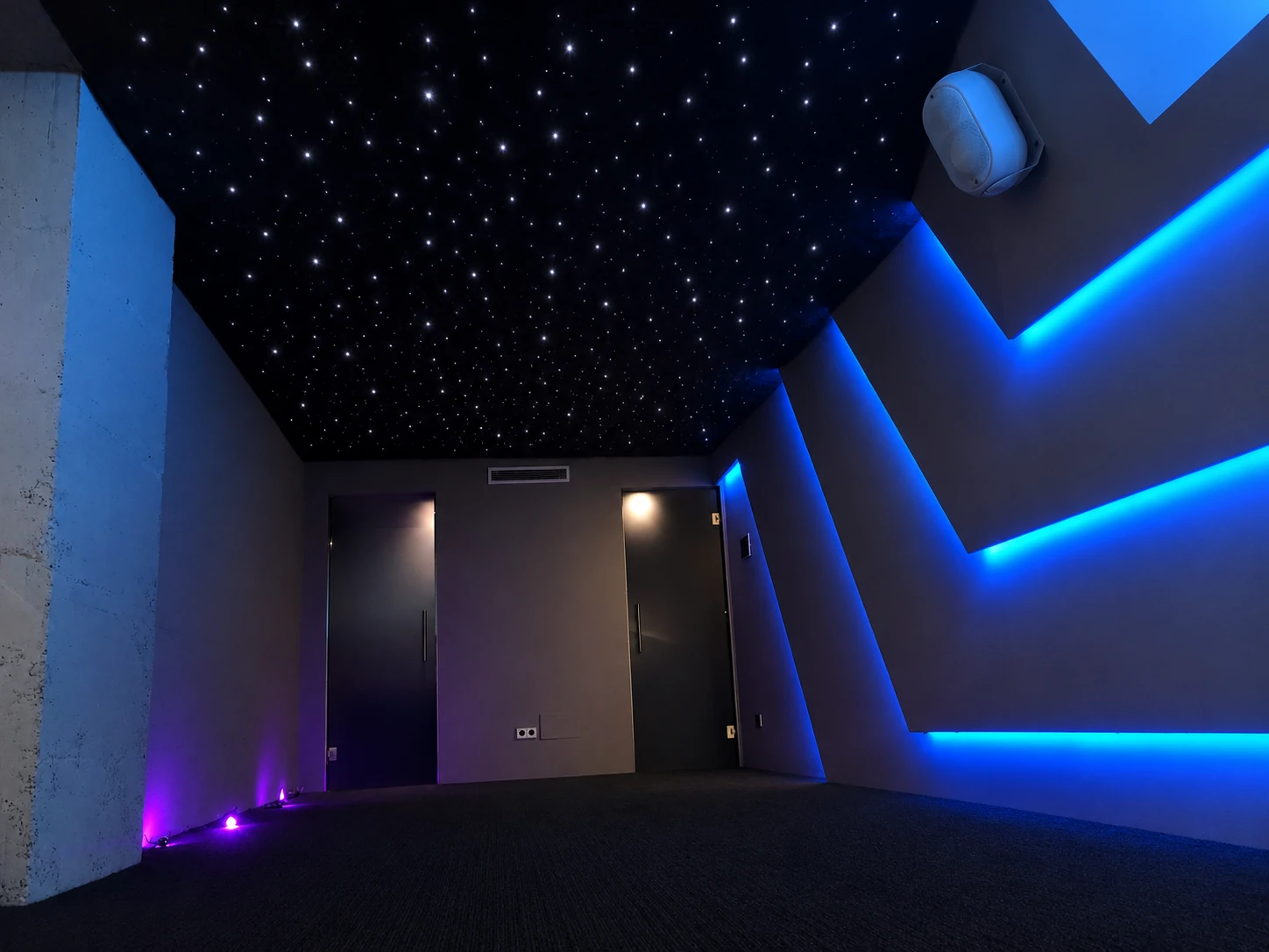 Cielo estrellado interior, moqueta negra y líneas LED azules en la pared derecha. Visualización editada sobre la fotografía original.