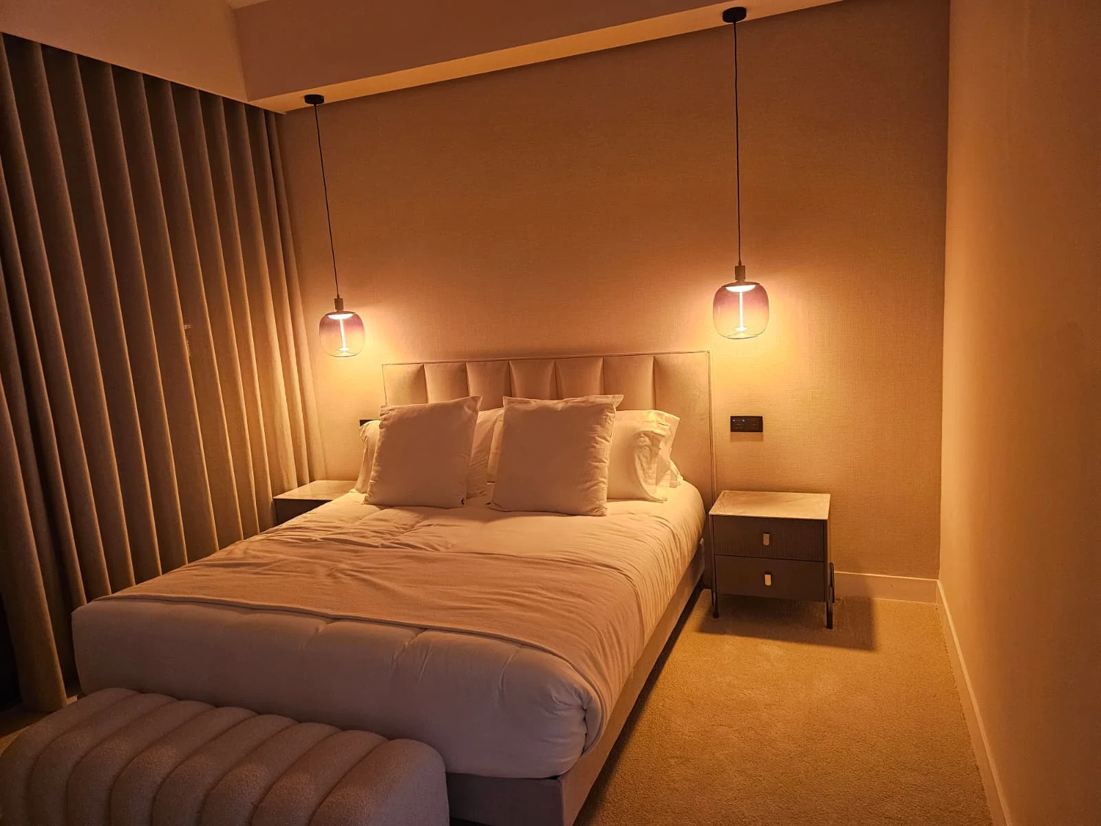 Dormitorio con luz cálida de ambiente y luminarias a ambos lados de la cama.