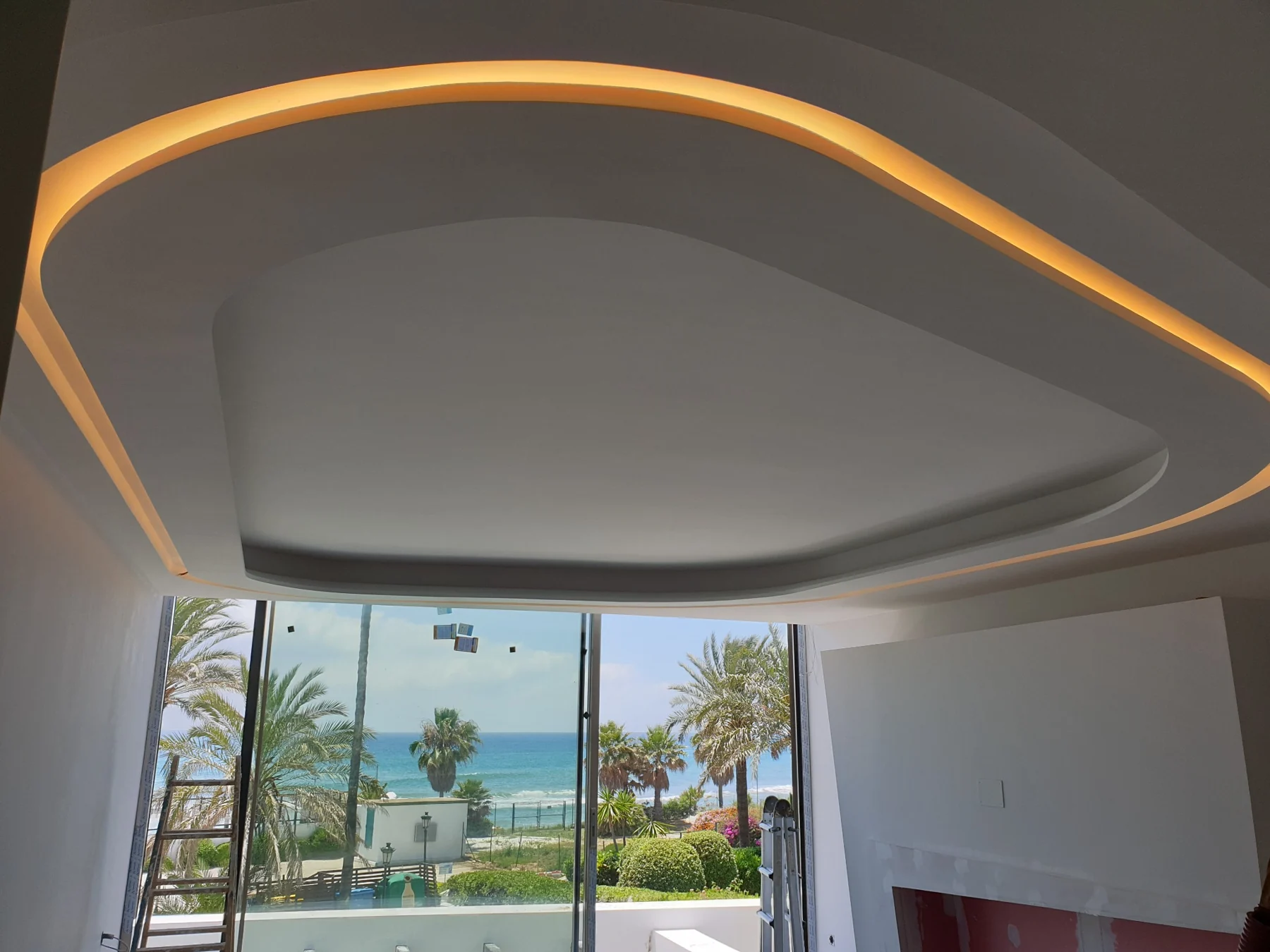 Foseado curvo con iluminación indirecta cálida junto a un gran ventanal.