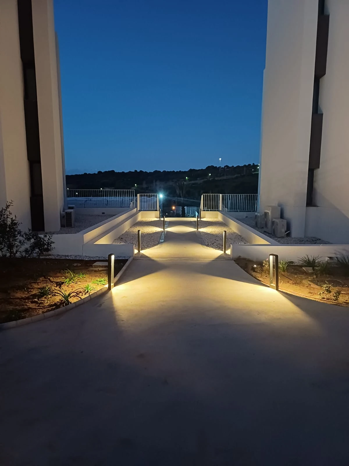 Iluminación de un camino exterior junto a una vivienda durante la noche.